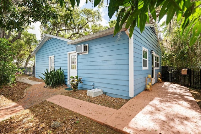 view of property exterior with a wall unit AC and fence