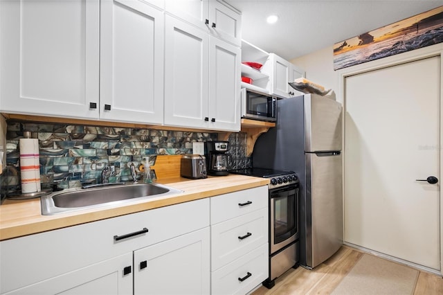kitchen with butcher block counters, white cabinets, a sink, stainless steel appliances, and decorative backsplash