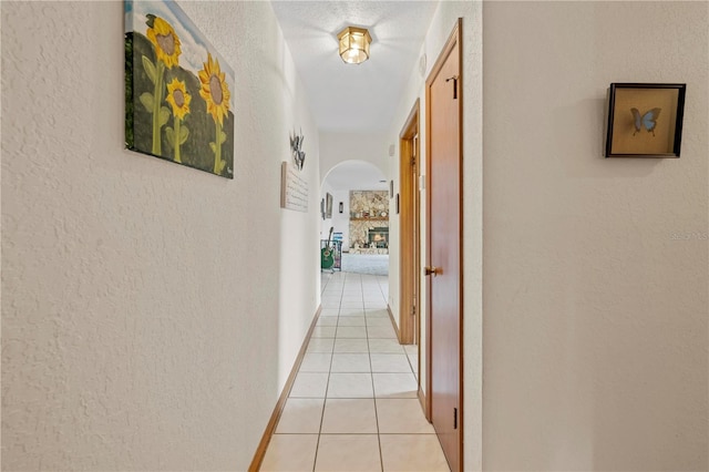 hallway featuring a textured wall, arched walkways, and light tile patterned flooring