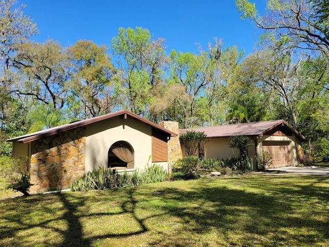 ranch-style home with a garage, stucco siding, a chimney, and a front yard