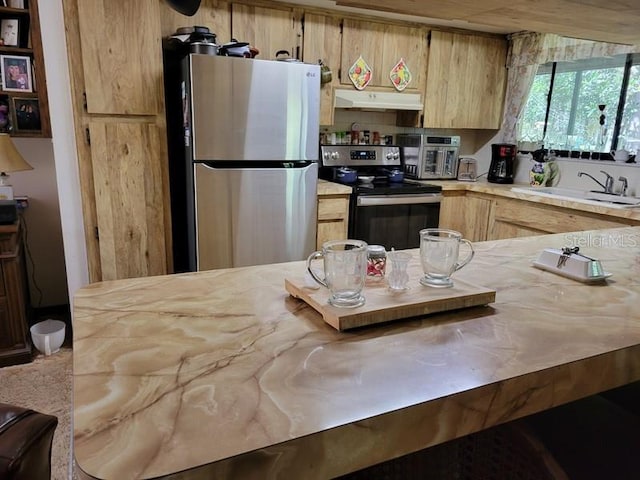 kitchen featuring light brown cabinetry, under cabinet range hood, a sink, light countertops, and appliances with stainless steel finishes