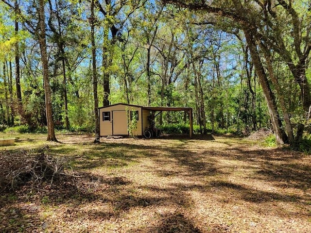 view of yard featuring an attached carport, an outbuilding, a wooded view, and a storage shed
