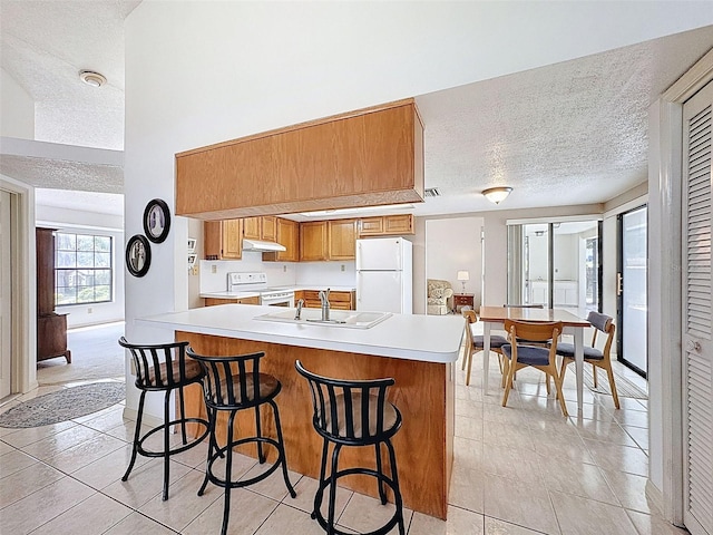 kitchen with light tile patterned floors, a textured ceiling, white appliances, and a sink