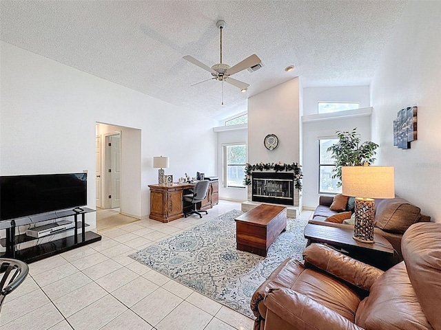 living area with a textured ceiling, light tile patterned flooring, a tiled fireplace, a ceiling fan, and high vaulted ceiling