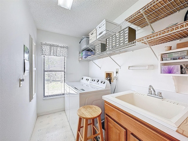 clothes washing area with a textured ceiling, a sink, washing machine and dryer, baseboards, and laundry area