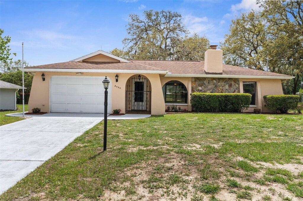 single story home with concrete driveway, stucco siding, a chimney, an attached garage, and a front yard
