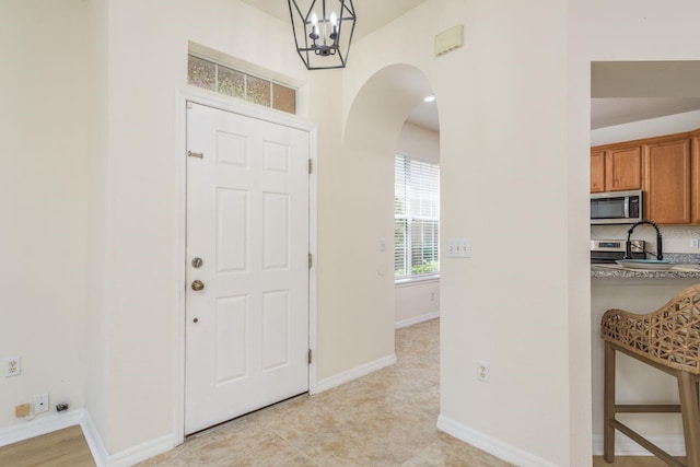 entryway featuring a chandelier, arched walkways, baseboards, and light tile patterned flooring