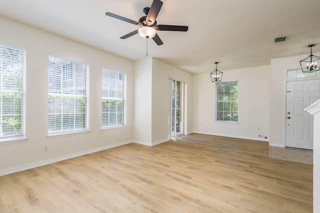 empty room with a chandelier, light wood finished floors, baseboards, and a ceiling fan