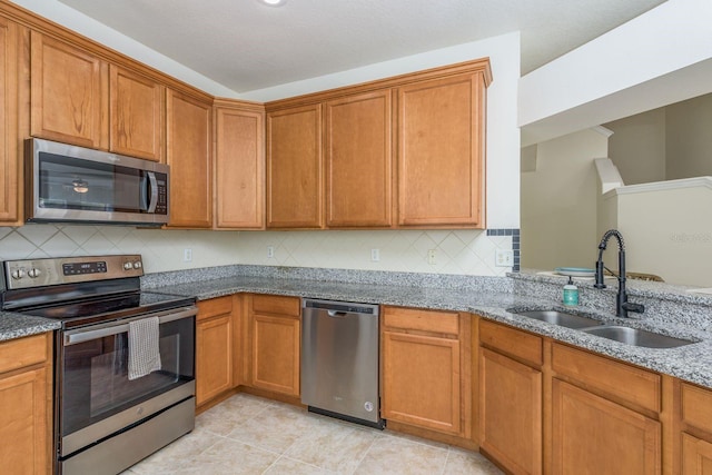 kitchen featuring appliances with stainless steel finishes, a sink, light stone countertops, and backsplash