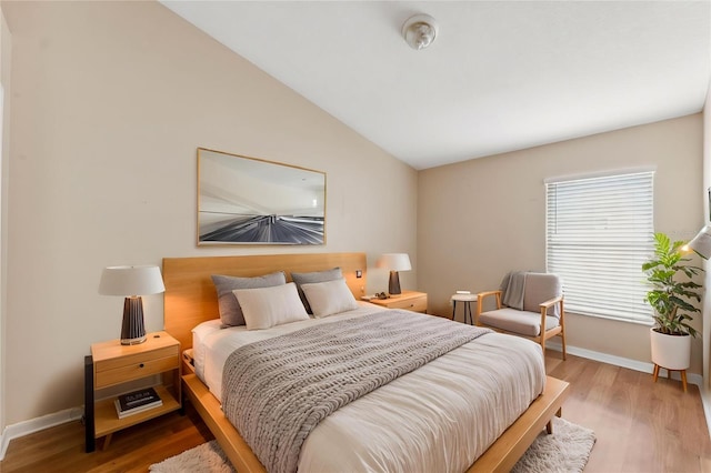 bedroom featuring baseboards, wood finished floors, and lofted ceiling