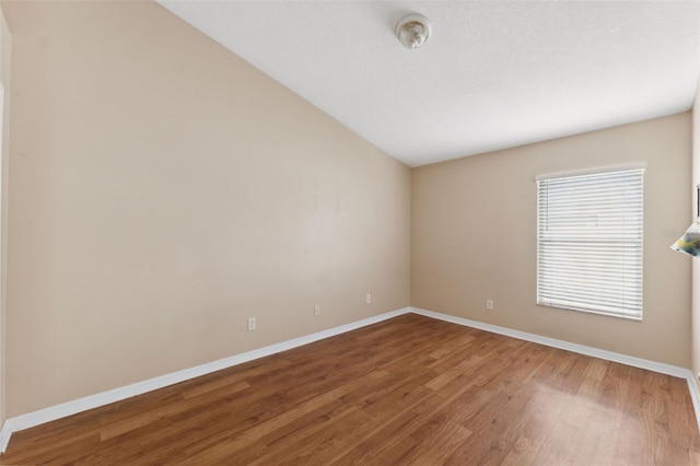 unfurnished room with wood finished floors, baseboards, and lofted ceiling