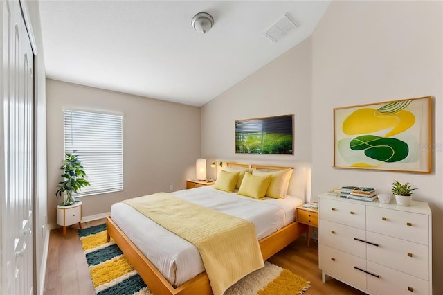 bedroom with light wood-style flooring, baseboards, vaulted ceiling, and visible vents
