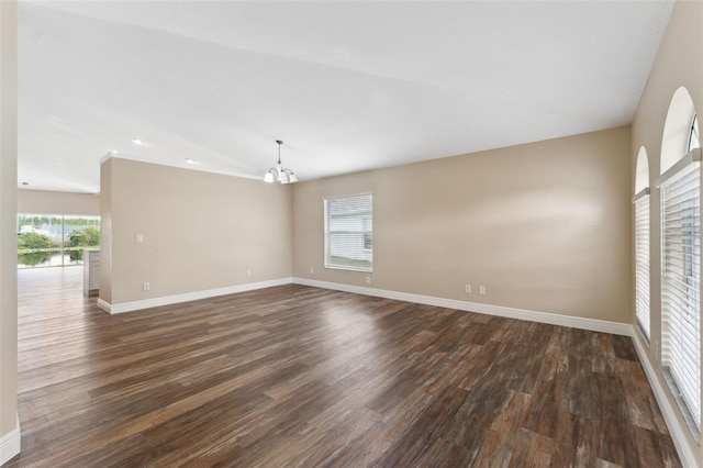 empty room featuring a chandelier, dark wood-style flooring, and baseboards