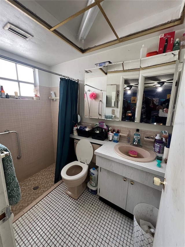 bathroom featuring toilet, vanity, visible vents, and tiled shower