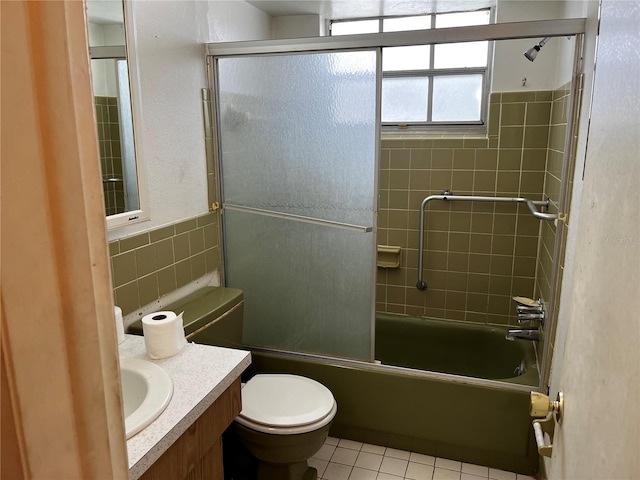 bathroom with shower / bath combination with glass door, tile patterned flooring, toilet, vanity, and tile walls