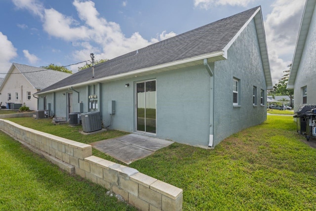 back of property with central air condition unit, a shingled roof, stucco siding, and a yard