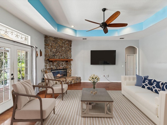 10318 Piper Dr, New Port Richey, FL 34654 - living room featuring a raised ceiling, arched walkways, wood finished floors, a ceiling fan, and a stone fireplace