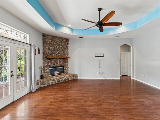 10318 Piper Dr, New Port Richey, FL 34654 - unfurnished living room featuring a raised ceiling, a ceiling fan, a stone fireplace, arched walkways, and wood finished floors