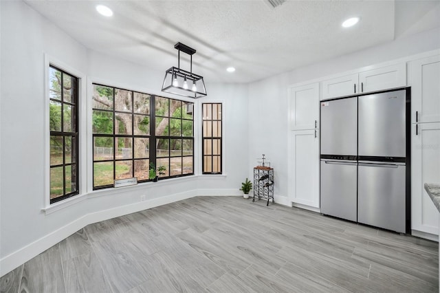 unfurnished dining area featuring a textured ceiling, light wood-style floors, baseboards, and recessed lighting