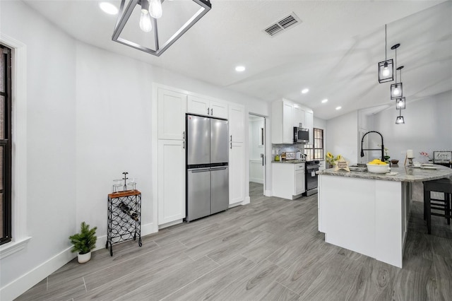 kitchen with pendant lighting, a kitchen bar, white cabinetry, visible vents, and appliances with stainless steel finishes