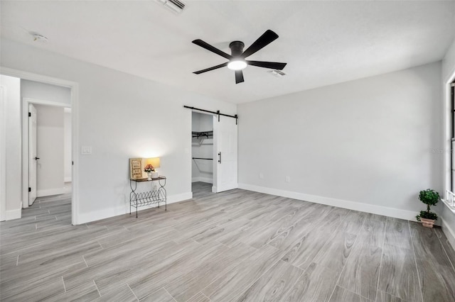 unfurnished bedroom featuring wood finished floors, baseboards, visible vents, and a barn door