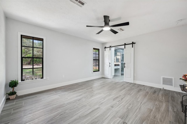 unfurnished bedroom with a barn door, visible vents, and multiple windows