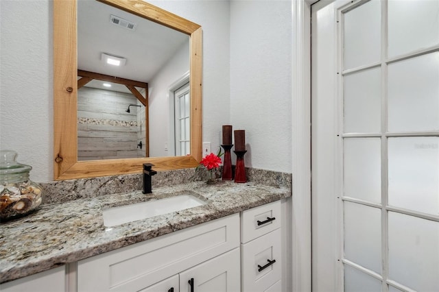 full bath with a textured wall, tiled shower, vanity, and visible vents