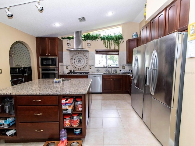 kitchen with light stone countertops, tasteful backsplash, wall chimney range hood, open shelves, and stainless steel appliances