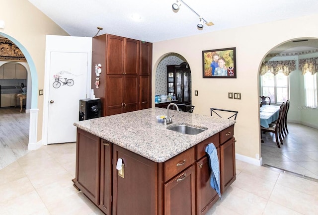 kitchen featuring arched walkways, a sink, light stone counters, and light tile patterned flooring