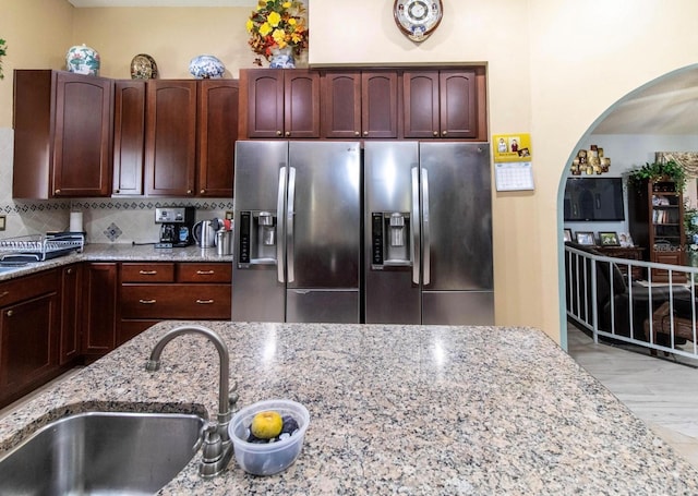 kitchen featuring a sink, light stone countertops, and stainless steel refrigerator with ice dispenser
