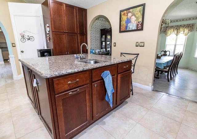 kitchen with arched walkways, light stone countertops, a sink, and light tile patterned flooring