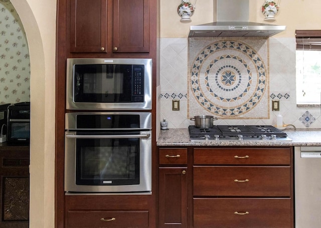 kitchen with stainless steel appliances, wall chimney exhaust hood, wallpapered walls, and decorative backsplash