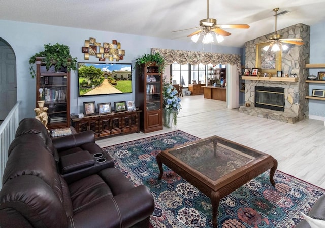 living room with arched walkways, a stone fireplace, ceiling fan, vaulted ceiling, and wood finished floors