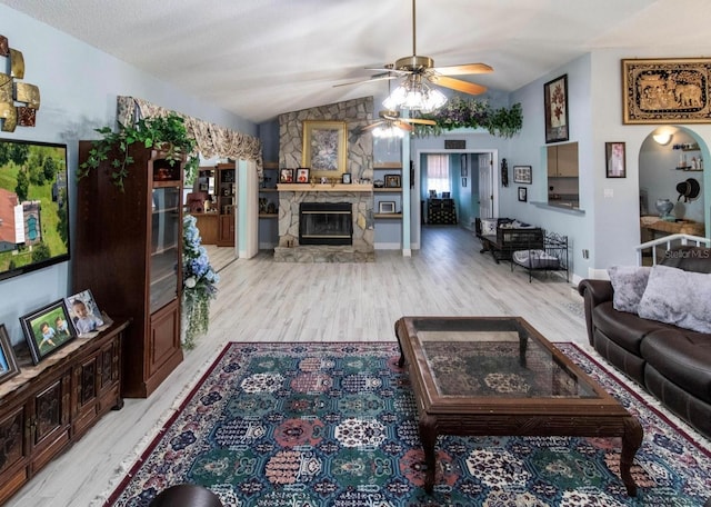 living area with light wood-style floors, ceiling fan, a fireplace, and vaulted ceiling
