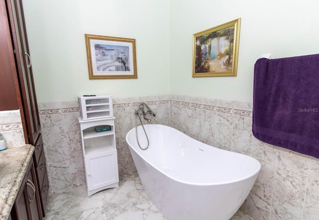 full bath with a freestanding bath, marble finish floor, tile walls, and a wainscoted wall