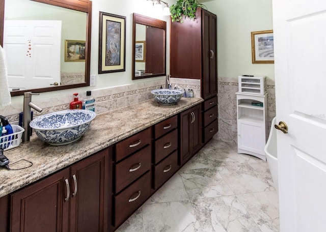 full bathroom featuring a wainscoted wall, marble finish floor, a sink, tile walls, and double vanity
