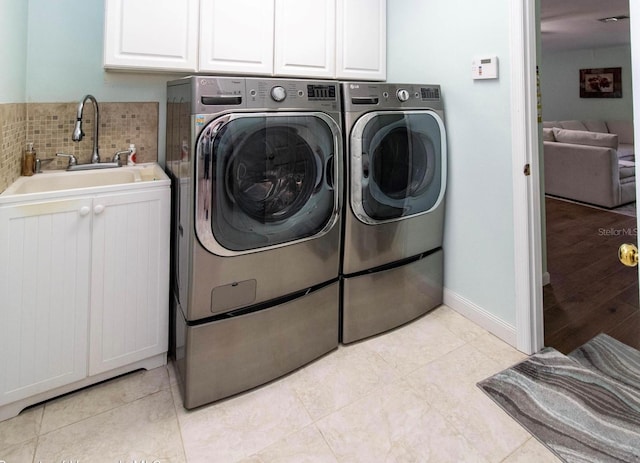 clothes washing area with light tile patterned flooring, a sink, washer and dryer, baseboards, and cabinet space