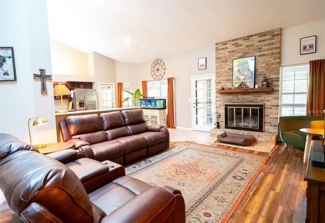 living area featuring a wealth of natural light, wood finished floors, a brick fireplace, and lofted ceiling
