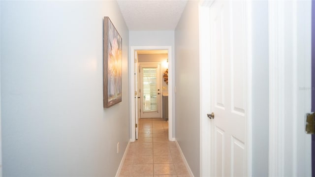 hall with a textured ceiling, light tile patterned flooring, and baseboards