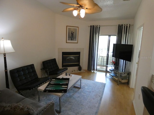 living room featuring a ceiling fan, a tiled fireplace, and wood finished floors