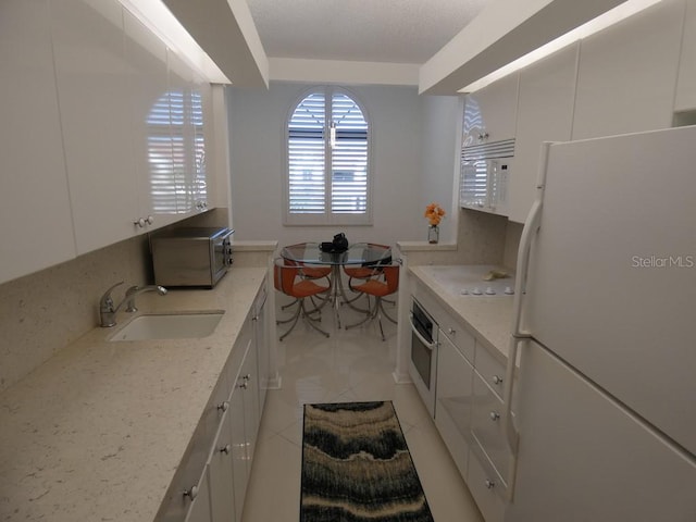 kitchen featuring light tile patterned floors, light stone counters, a sink, white cabinetry, and stainless steel appliances