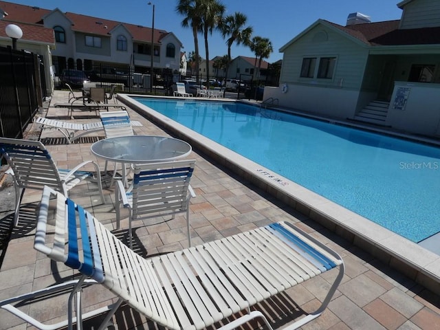 community pool with a patio, fence, and a residential view