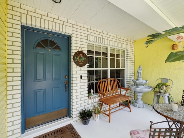 view of exterior entry featuring brick siding and covered porch
