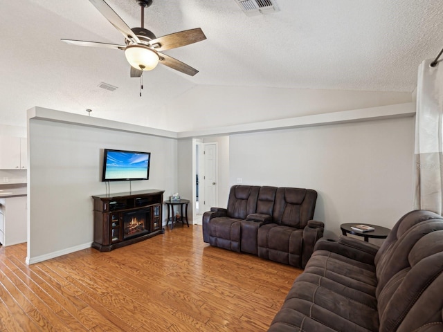 living room featuring lofted ceiling, wood finished floors, visible vents, a ceiling fan, and a textured ceiling