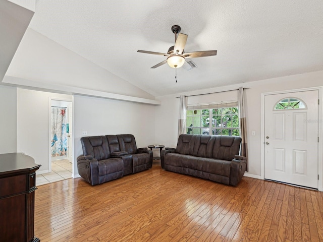 living area with a textured ceiling, light wood-type flooring, visible vents, lofted ceiling, and ceiling fan
