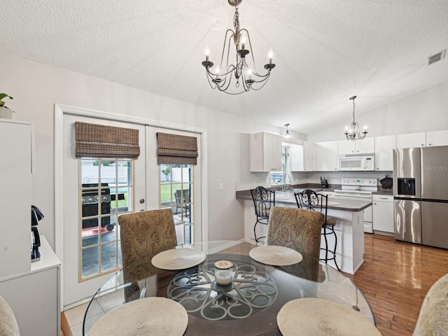 dining area with vaulted ceiling, visible vents, a chandelier, and a textured ceiling