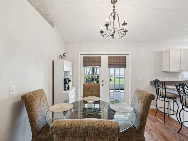dining space featuring wood finished floors, a textured ceiling, a notable chandelier, and french doors