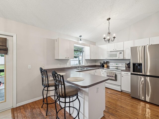 kitchen featuring dark countertops, a sink, a textured ceiling, white appliances, and a peninsula
