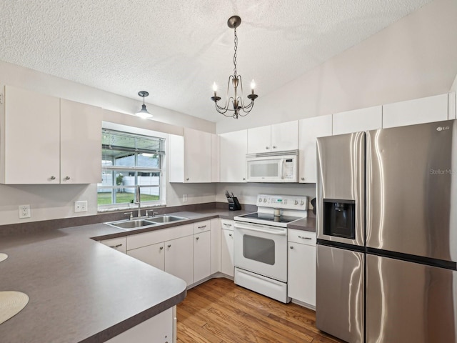 kitchen featuring an inviting chandelier, dark countertops, a sink, white appliances, and a textured ceiling