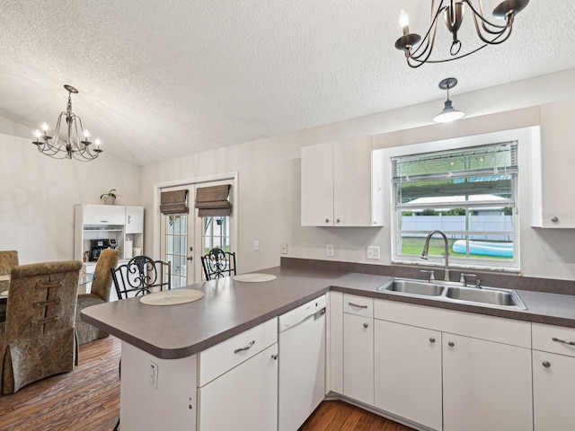 kitchen with a peninsula, a textured ceiling, a sink, a chandelier, and white dishwasher